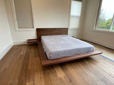 a bed sitting on top of a hard wood floor in a bedroom next to a window