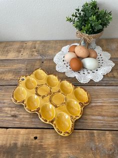 an egg tray on a wooden table next to some eggs and a potted plant