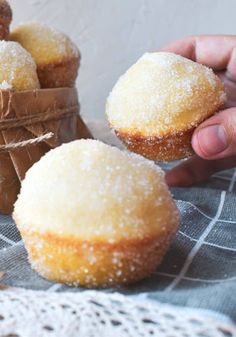 a person holding a sugared doughnut in front of other pastries on a table