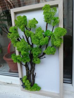 there is a fake tree made out of wood and moss in the frame on the window sill