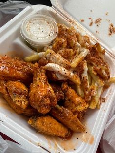 a takeout container filled with chicken wings and french fries next to a dipping sauce