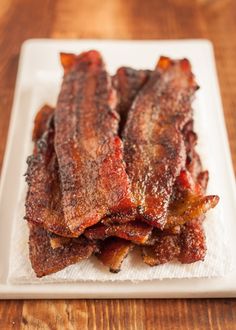 bacon on a white plate sitting on top of a wooden table