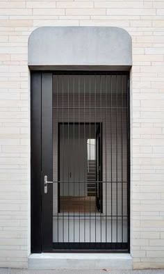 a black door with bars on it and a brick wall in the background, behind which is an open doorway