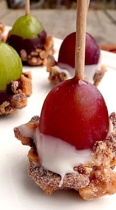 several desserts are arranged on a white plate with wooden skewers and grapes