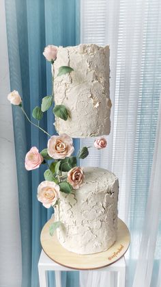 a three tiered white cake with flowers on the top and bottom, sitting on a wooden stand