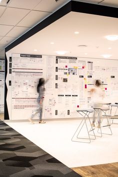 two people standing in front of a wall with papers on it and one person riding a skateboard