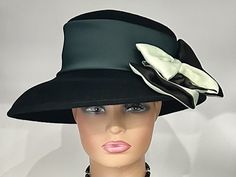 "The featured hat is a  black colored wool winter dress hat.   It has a wide silk band in a forest green color. A gorgeous two tone  bow in black and sage green is placed on an angle. This bow is elegant and classy. The combination of different textures and colors is what makes this hat so charming and disarming. The softness of the bow on the solid black hat is a striking look! This hat can be worn as a winter Church Hat, a Wedding Party Hat, a Tea Party hat,  a Downton Abbey  hat,  winter hat Fitted Brimmed Hat With Bow, Formal Black Winter Top Hat, Formal Black Cloche Hat For Winter, Black Formal Winter Cloche Hat, Fitted Wide Brim Hat With Bow, Winter Party Hats With Bow, Winter Evening Top Hat With Curved Brim, Fitted Black Wool Cloche Hat, Evening Winter Top Hat With Curved Brim