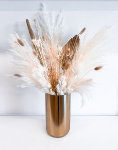 there is a vase with feathers in it on the table next to a white wall