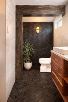 a bathroom with a toilet, sink and wood paneled walls in the background is a potted plant