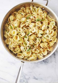 a pan filled with pasta and vegetables on top of a marble countertop next to a silver spatula