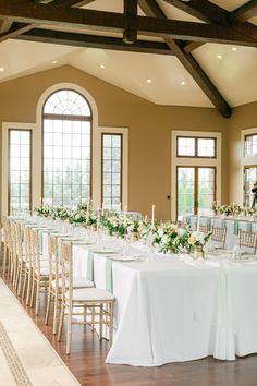 a long table with white linens and greenery is set up for a formal function