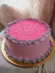 a pink and purple cake sitting on top of a gold plate next to a window