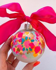 a hand holding a christmas ornament with a pink bow on it's side