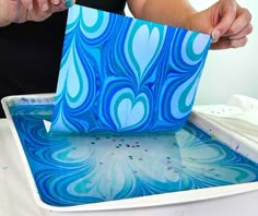 a person is cutting paper into a blue and white design on a tray with watercolors