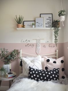 a white bed topped with lots of pillows next to a shelf filled with potted plants