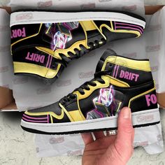 a hand is holding up a pair of black and yellow sneakers with pink lettering on them