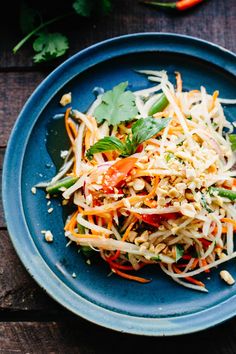 a blue plate topped with salad on top of a wooden table next to an orange and green pepper