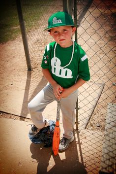 a young boy holding a baseball bat on top of a dirt field next to a fence