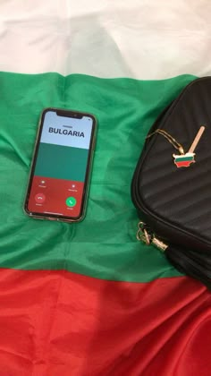 a cell phone sitting on top of a green and red blanket next to a black purse