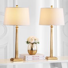 two lamps sitting on top of a table next to books and a vase with flowers