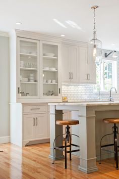 a large kitchen with white cabinets and wood flooring on the wooden floor, along with two bar stools