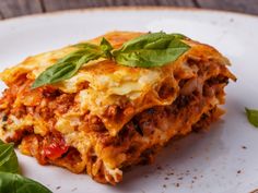 a white plate topped with lasagna covered in meat and cheese, garnished with basil