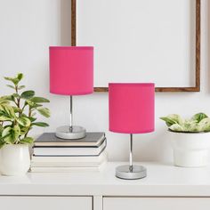 two pink lamps sitting on top of a white dresser next to a mirror and potted plant