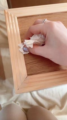 a person with their hand on a piece of paper in a wooden frame that is sitting on a bed