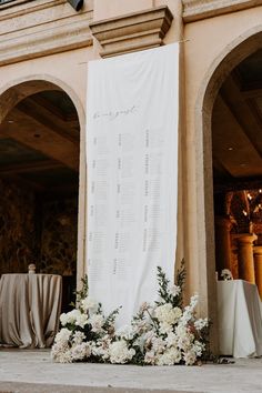 a wedding ceremony setup with white flowers and greenery in front of a large sign