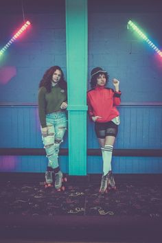 two women standing next to each other in front of a blue wall with neon lights