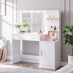 a white vanity table with drawers and mirror next to a potted plant on the floor