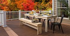 a table and bench on a deck with trees in the background