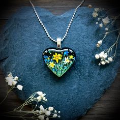 a heart shaped glass pendant with flowers on it sitting on a rock next to some white flowers