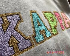 "Chenille Style Glitter Letters, Sorority Crew Neck Sweatshirt, Chenille Style Letters with Gold Glitter Backing Our comfy and adorable Chenille Style Letters on your favorite color Crewneck Sweatshirt is the perfect throw on piece! Choose your Sorority, color thread and your color sweatshirt!  Letters do not come in Greek Alphabet. Choose Your Thread Color for Interior of Letters.  The backing will be Gold Glitter. Shown in Bright Multi Color Scheme with Lavender, Teal, Lime, Pink, Blush Pink Letter size is determined by number of letters on sweatshirt. Total embroidery width will be 13\". 4 Letters on Kappa Sweatshirt are 2 3/4\" 3 Letters will be approx. 3 1/4 \" 50% cotton, 50% polyester NuBlend preshrunk fleece Unisex Fit S,M,L New Cropped Hoodie Style 8.3-ounce, 65/35 ring spun cotto Kappa Sweatshirt, Letters Sorority, Style Letters, Sorority Sweatshirts, Color Sweatshirt, Greek Alphabet, Glitter Letters, Hoodie Style, Pink Letter