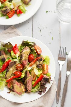 two white plates filled with meat and vegetables on top of a table next to silverware