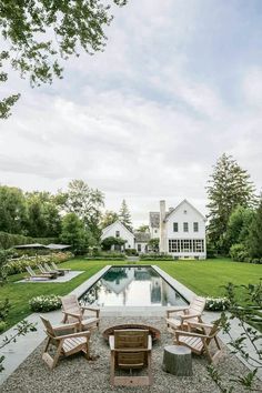 an outdoor fire pit with chairs around it and a house in the background, surrounded by greenery