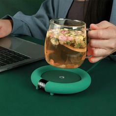 a woman is holding a glass with tea in it while sitting at a table next to a laptop