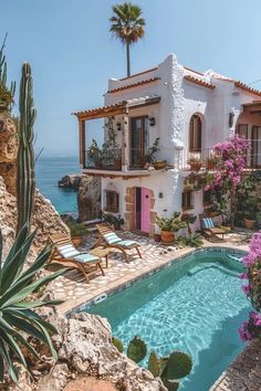 a house with a pool in front of it next to the ocean and cactus trees