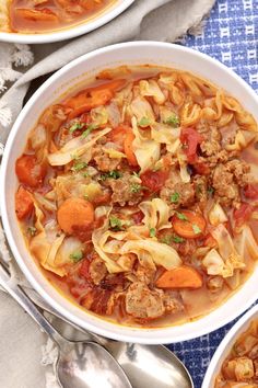 two bowls filled with meat and noodles on top of a blue table cloth next to silver spoons