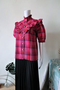 Cute French Vintage short sleeve blouse from the 1980s. Pie crust collar, straight cut. Beautiful Madras check pattern with pink, red, blue and yellow tones. Ruffle bib and yoke. Short puff sleeves with buttoned cuffs. Side vents. Made in France! BRAND: Daniel Duval Paris ERA: 1980s COLOR: Pink, red, yellow, purple, blue FABRIC: 65% polyester, 35% cotton SIZE: Vintage size 40 (FR), fits best size M (or size S for an oversized fit) - for reference please check the measurements below MEASUREMENTS: Short Sleeve Plaid Tops With Ruffles, Plaid Short Sleeve Tops With Ruffles, Plaid Short Sleeve Blouse For Work, Vintage Short-sleeve Blouse With Ruffles, Retro Short Sleeve Plaid Blouse, Retro Plaid Short Sleeve Blouse, Check Blouse, Checked Blouse, Vintage Short