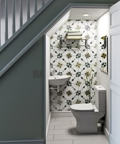 a white toilet sitting under a stair case next to a bathroom sink and toilet paper