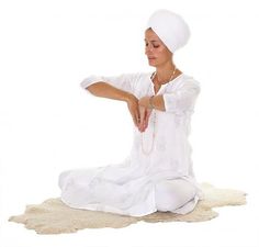 a woman sitting on the ground in a white outfit doing yoga exercises with her hands