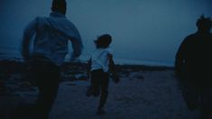 three people are running on the beach at night, one is wearing a white shirt