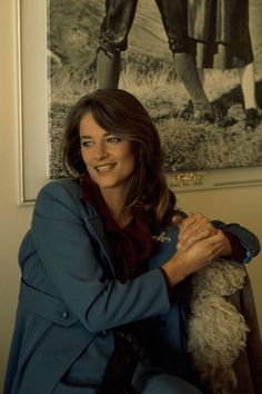 a woman sitting on a chair holding a dog in front of a horse photo hanging on the wall