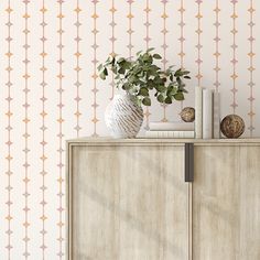 a white vase sitting on top of a wooden cabinet next to a wallpapered wall