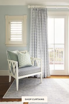 a white chair sitting in front of a window next to a blue rug on top of a hard wood floor