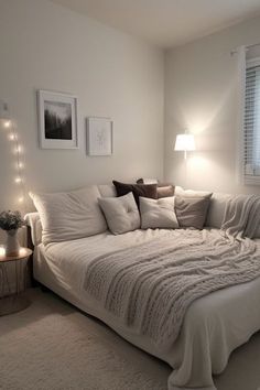 a white bed sitting in a bedroom next to a window covered in blankets and pillows