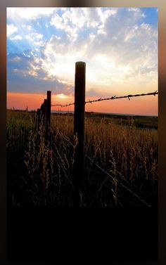 the sun is setting behind a barbed wire fence in an open field with tall grass