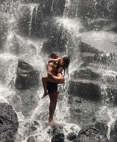 a man and woman are kissing in front of a waterfall while standing on the rocks