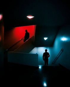 a man standing in the dark next to an escalator with red and blue lights